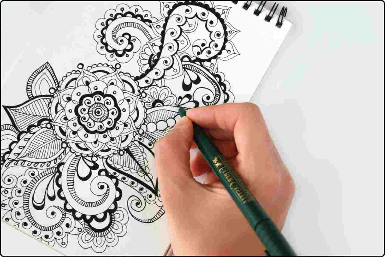 A person holding a black pen, sketching a detailed flower on white paper.